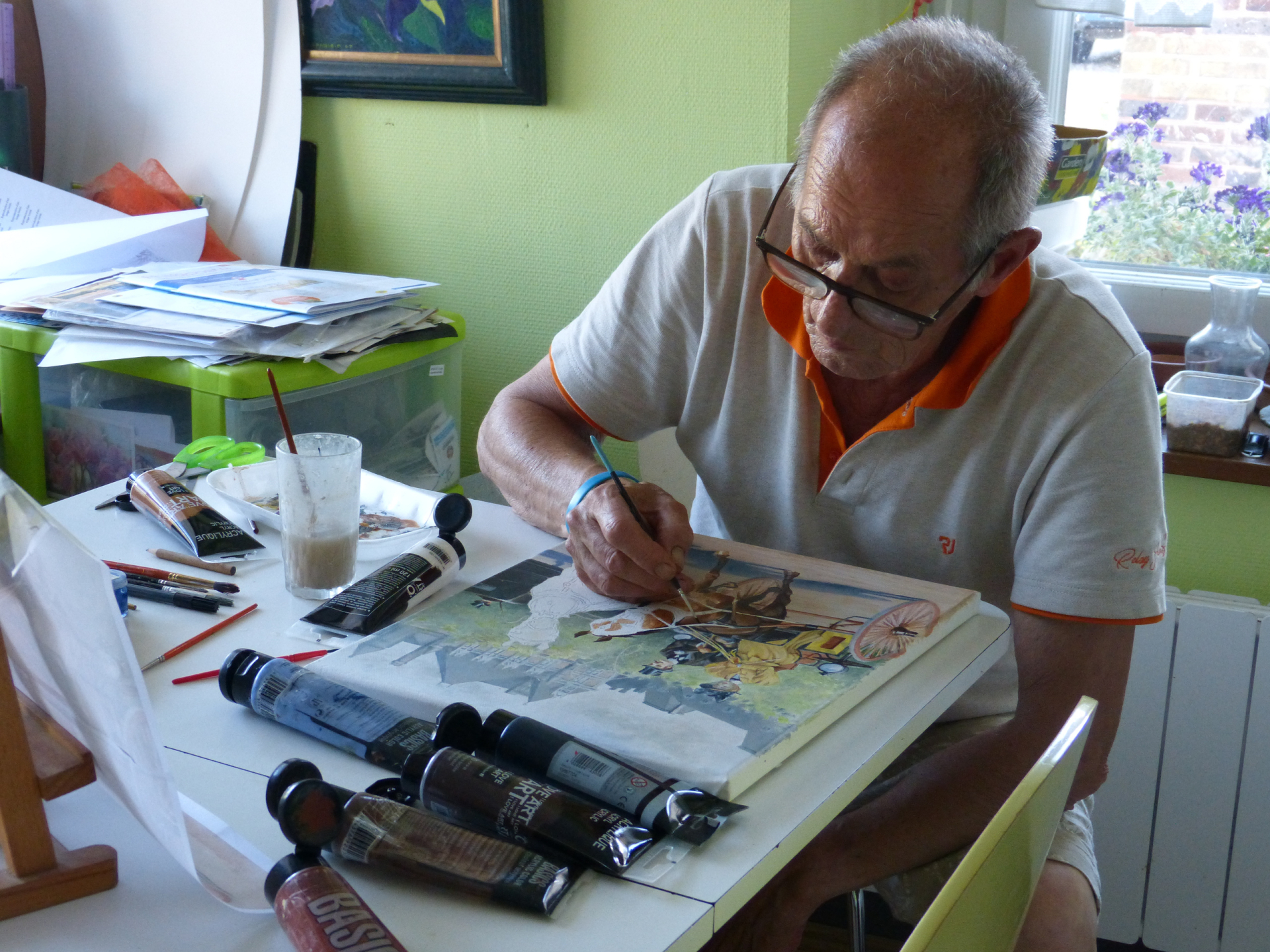 Jean-Louis Aparicio, assis à sa table, peint à l’acrylique une calèche tirée par un cheval sur une toile encore inachevée.
